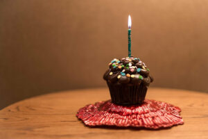 single chocolate cupcake with a green candle in it. On a table and on a red mat.