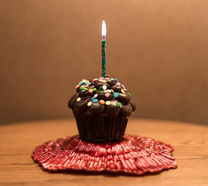 single chocolate cupcake with a green candle in it. On a table and on a red mat.